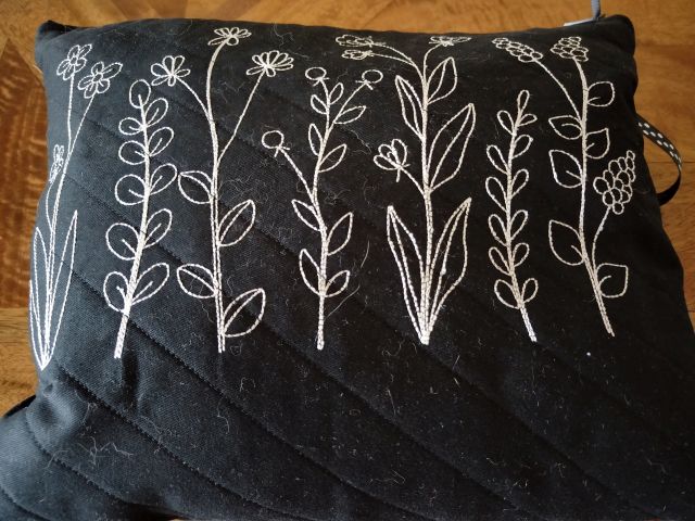 Image of a black quilted zipper bag with white flowers embroidered on it.